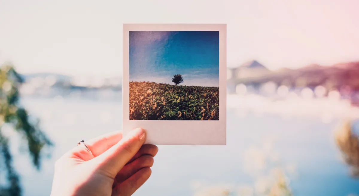 A hand holding up an instant photo print against a soft blurred background