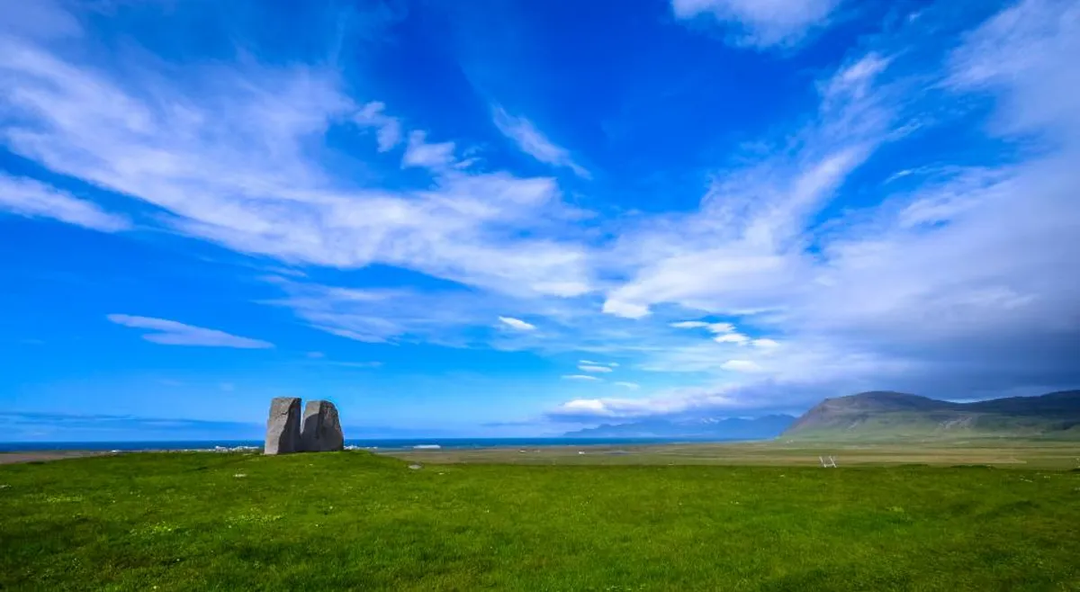 A wide blue sky with streaks of white cloud over a green field