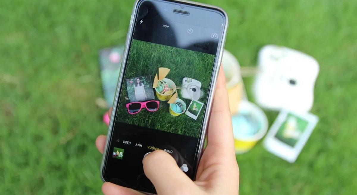 A hand holding a phone that shows a photo of instant prints on the grass